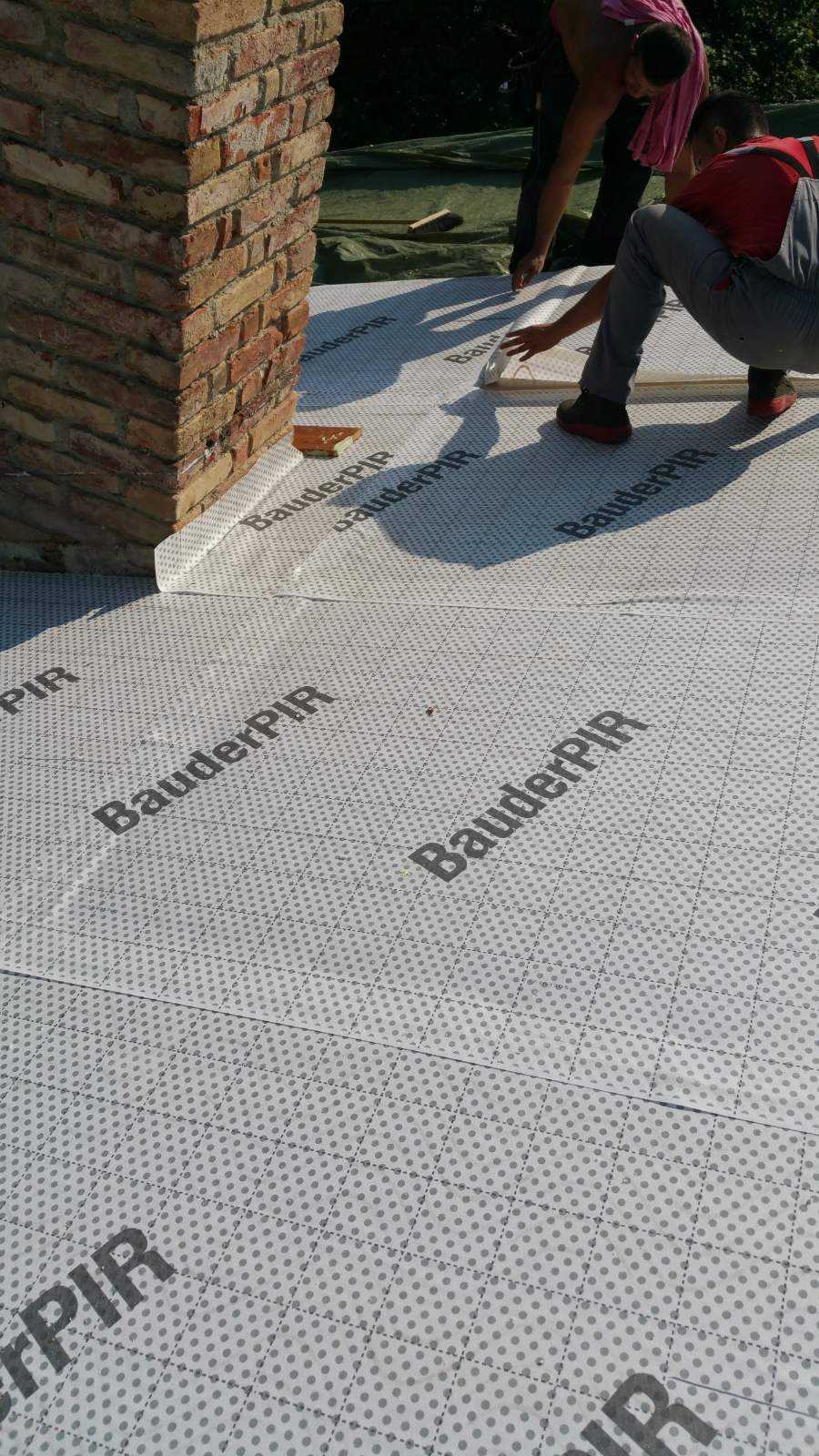 PIR-Dämmplatten auf einem Flachdach neben einem Kamin, ein Handwerker bei der Arbeit