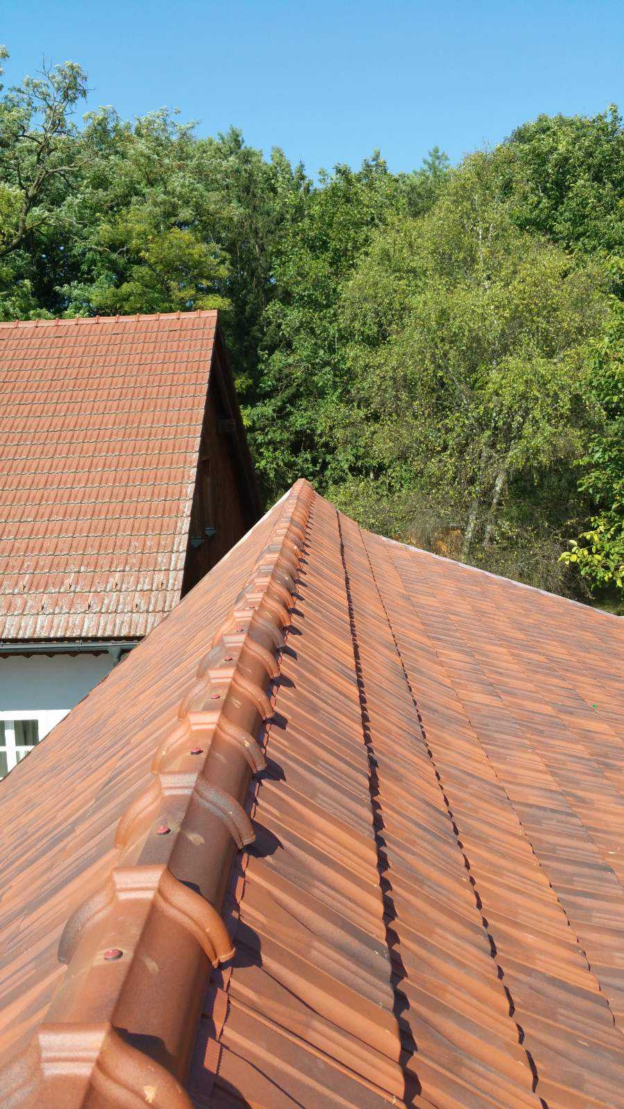 First eines neu gedeckten Ziegeldachs vor grünen Bäumen